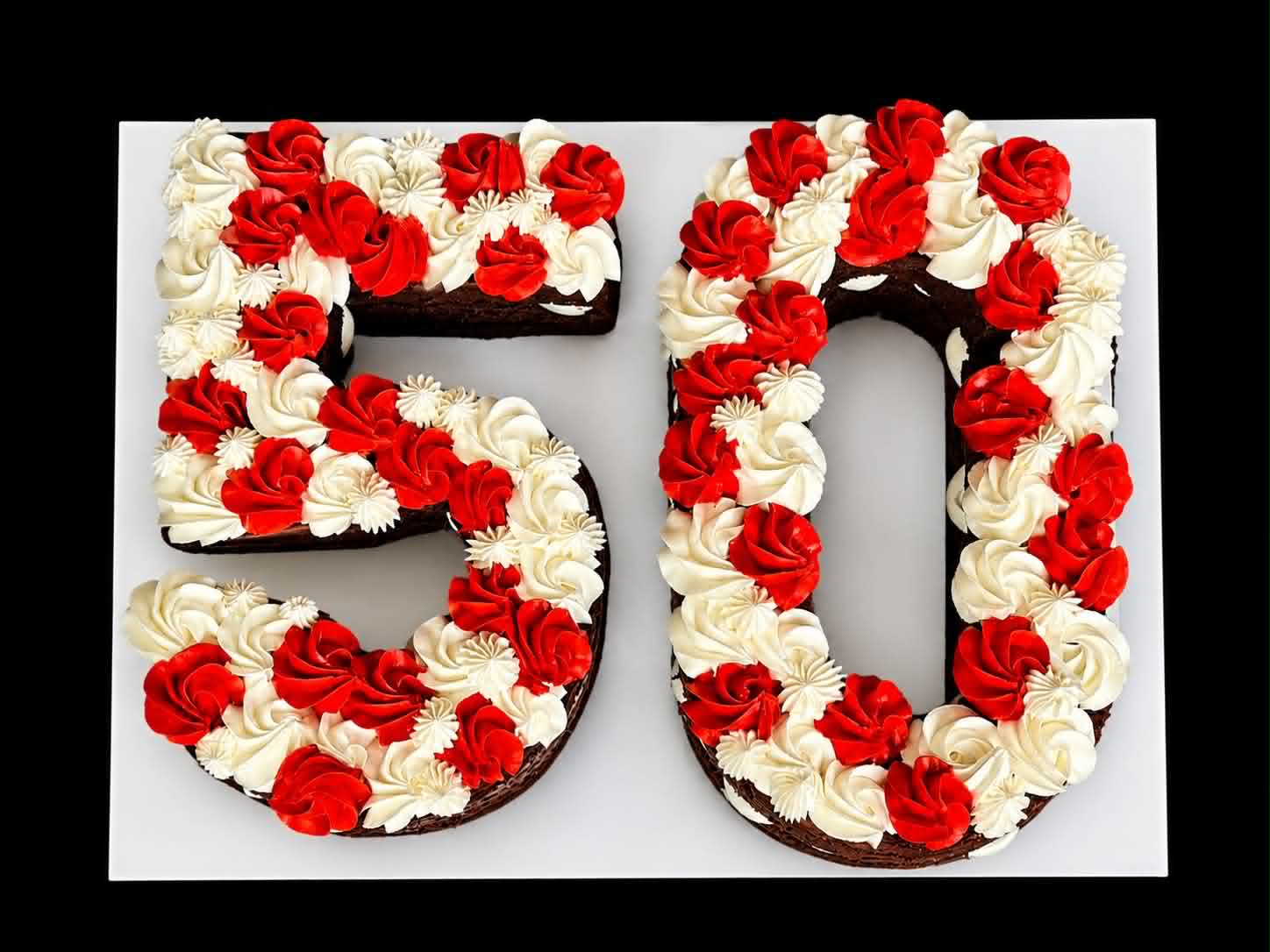 Number 50 shaped cake with red and white buttercream rose rosettes on chocolate sponge